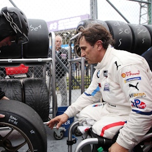 Alessandro Zanardi sitzt in Rollstuhl und greift nach einen Autoreifen.