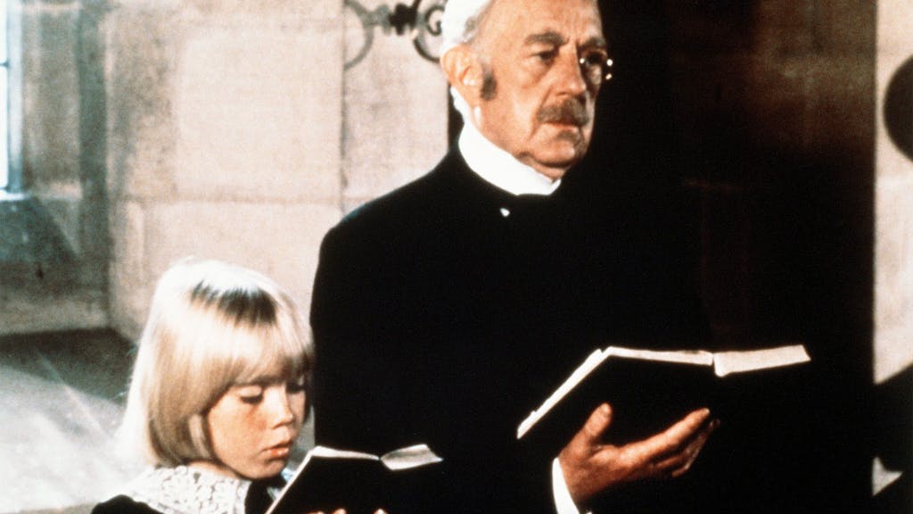 Der alte Earl of Dorincourt (Alec Guinness) steht neben seinem Enkel Ceddie (Ricky Schroder). Beide halten ein Gesangsbuch in der Hand.&nbsp;