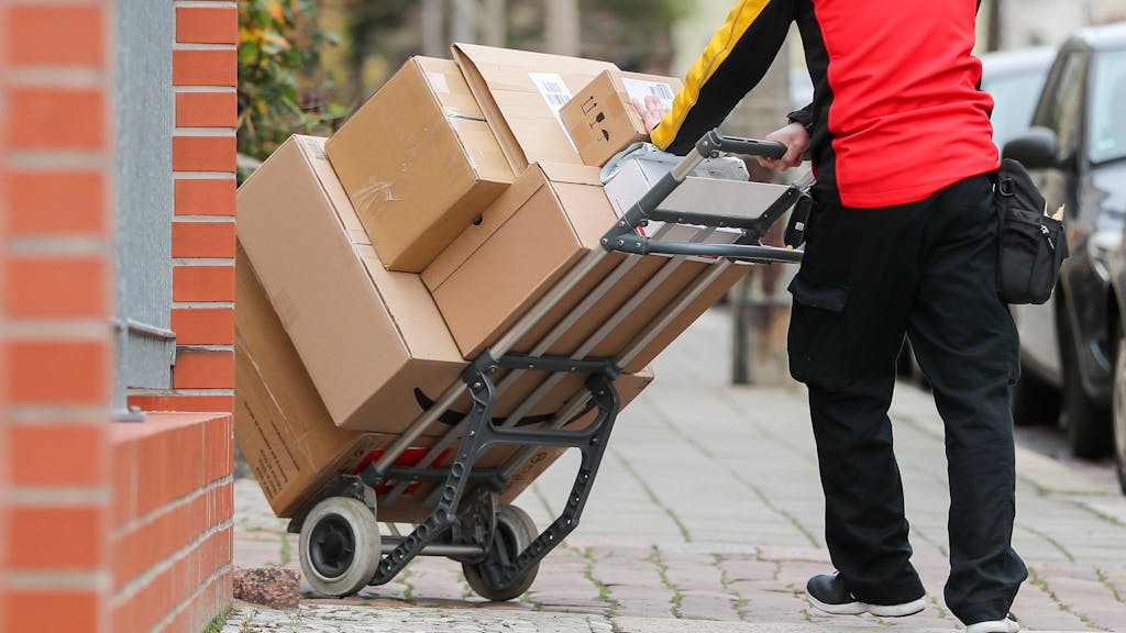 Ein Paketzusteller geht mit einer Sackkarre voller Pakete zu einem Haus.