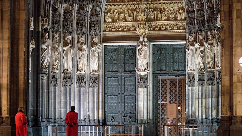Zwei Domschweizer stehen am frühen Morgen auf der Domplatte vor dem Eingang Hauptportal des Doms.