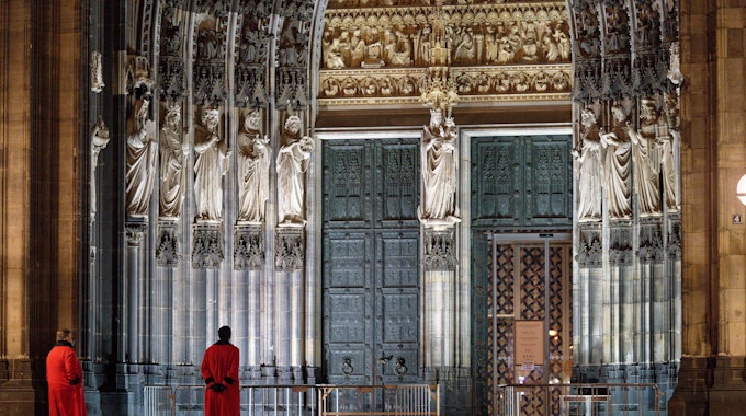 Zwei Domschweizer stehen am frühen Morgen auf der Domplatte vor dem Eingang Hauptportal des Doms.