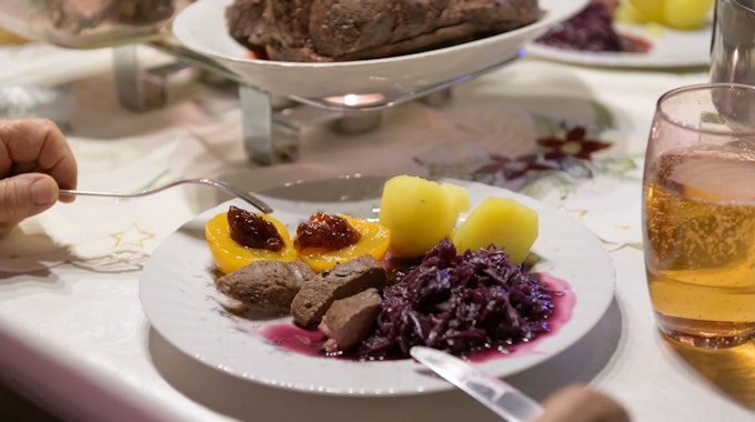 Hamburg: Damhirsch-Rücken mit Kartoffeln und Rotkohl sowie Preiselbeergelee auf Aprikosen liegen verzehrfertig auf einem Teller an Heiligabend.