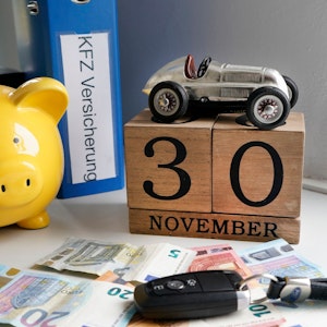 Auf dem Foto sieht man mehrere Geldscheine, ein gelbes Sparschwein, ein Autoschlüssel und einen Aktenordner.