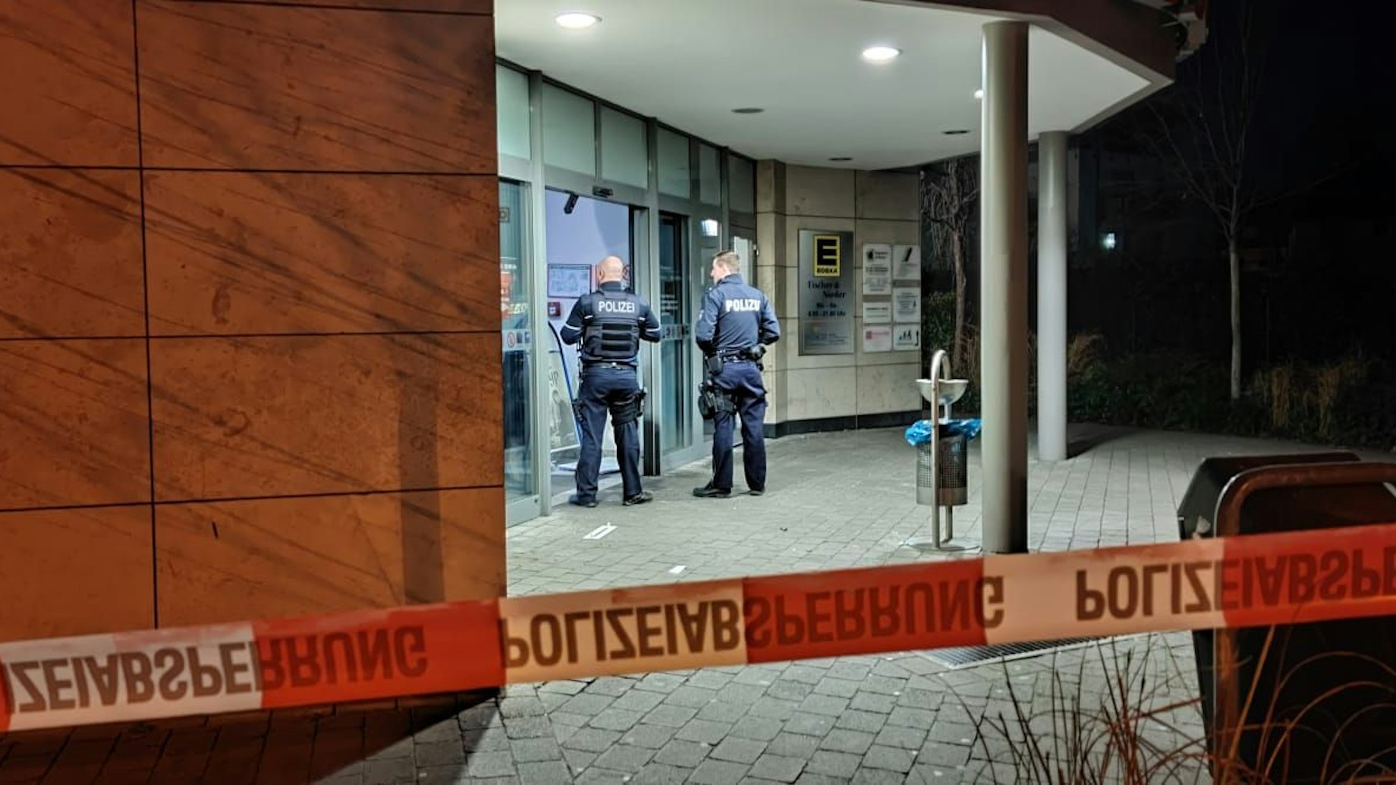 Zwei Polizisten stehen vor einer Bankfiliale, die mit Flatterband abgesperrt ist.