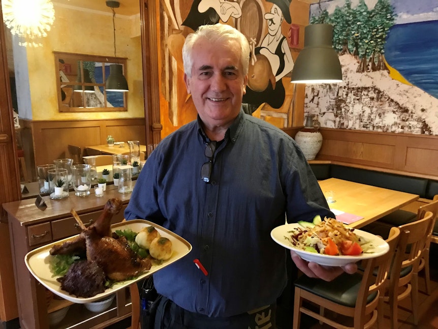 Christos Spanos steht mit zwei Gerichten auf Tellern im Restaurant.