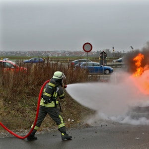 Ein Feuerwehrmann löscht mit einen Wasserschlauch einen Wagen, der in Flammen steht.