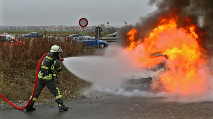 Ein Feuerwehrmann löscht mit einen Wasserschlauch einen Wagen, der in Flammen steht.