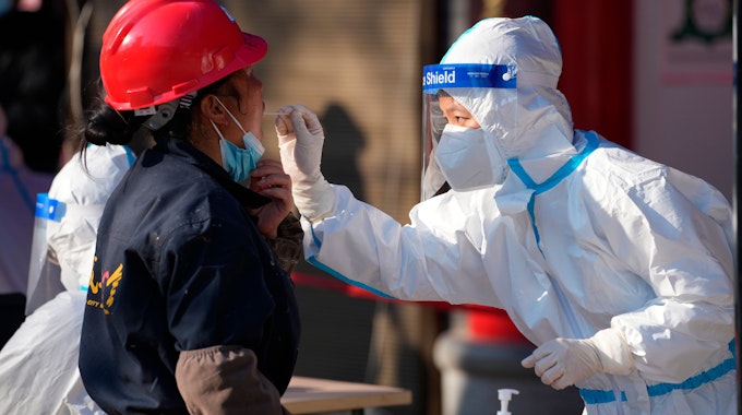 China, Xi'an: Eine Mitarbeiterin in einem medizinischen Schutzanzug entnimmt einer Frau an einer Corona-Teststation in der Provinz Shaanxi einen Abstrich über den Mund.&nbsp;