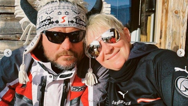 Steffen Baumgart sitzt mit seiner Frau Katja, Sonnenbrille und Hörner-Mütze an einer Skihütte in Österreich.