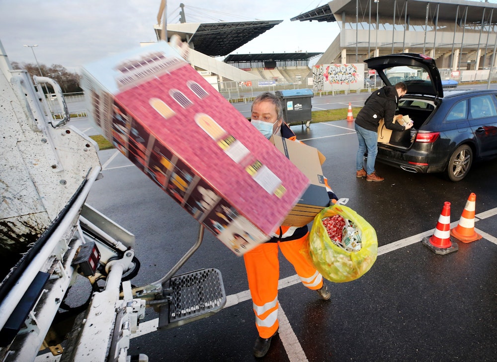 Geschenkpapier und -Kartons wirft ein Mitarbeiter der Entsorgungsbetriebe Essen in einen Müllwagen.