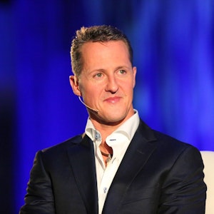 Michael Schumacher sitzt auf einem Stuhl. Er trägt Hemd und Anzug.