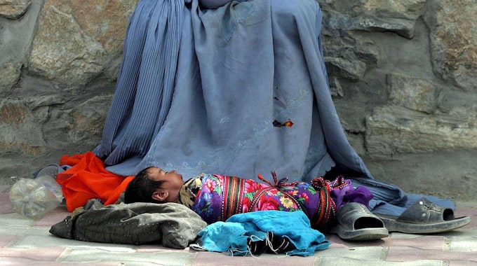 Eine Afghanin bettelt am Straßenrand um Almosen, ihr Säugling liegt vor ihr.