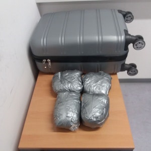 Vier Päckchen mit Drogen liegen vor einem Koffer auf einem Tisch.