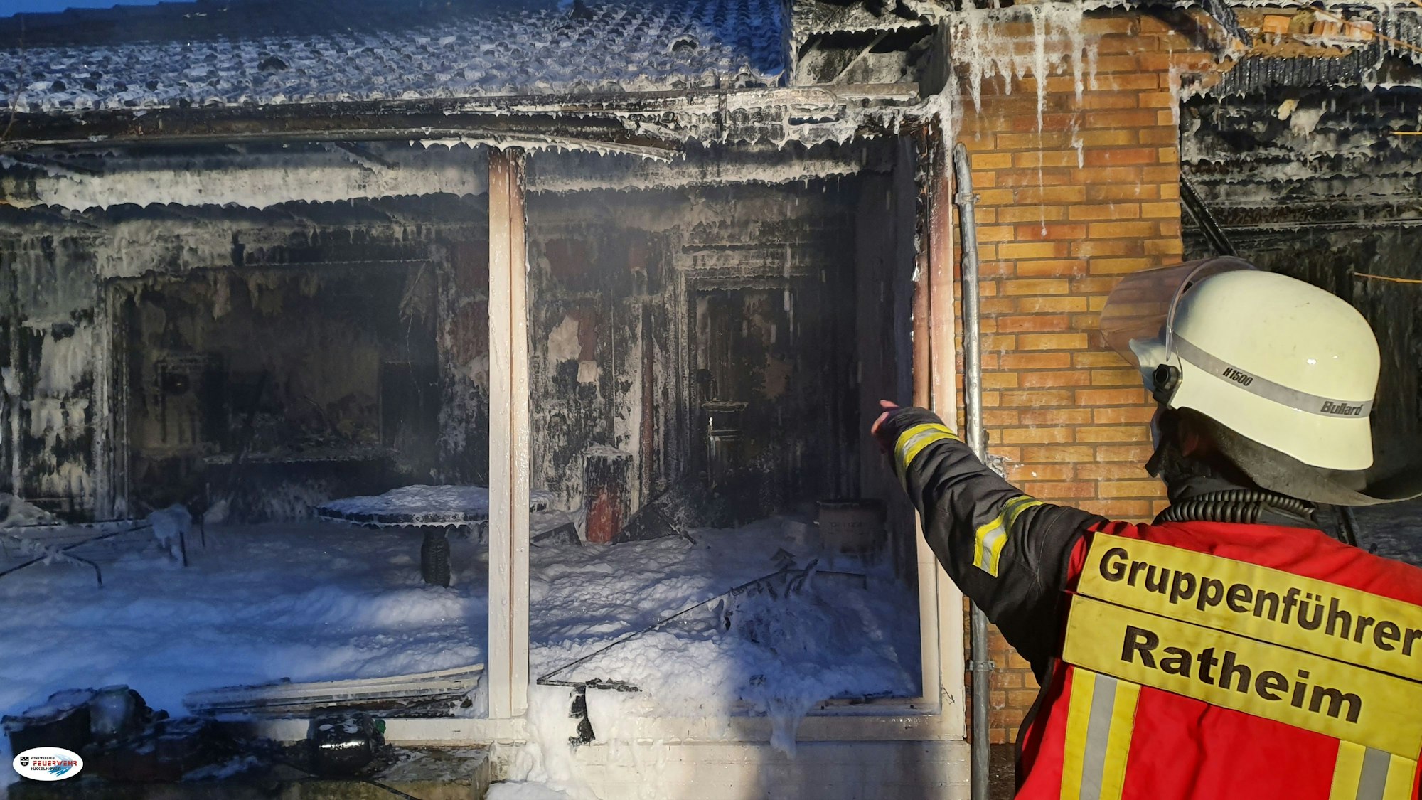 Ein Feuerwehrmann zeigt auf einen ausgebrannten Raum, in dem Löschschaum steht.