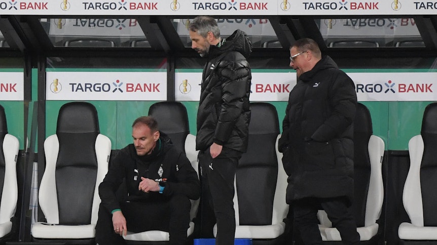 Gladbach-Manager Max Eberl (r,), Trainer Marco Rose (M.) und Co-Trainer Alexander Zickler (l.) blicken sichtlich enttäuscht nach der Pokal-Pleite gegen Dortmund am 2. März 2021drein.