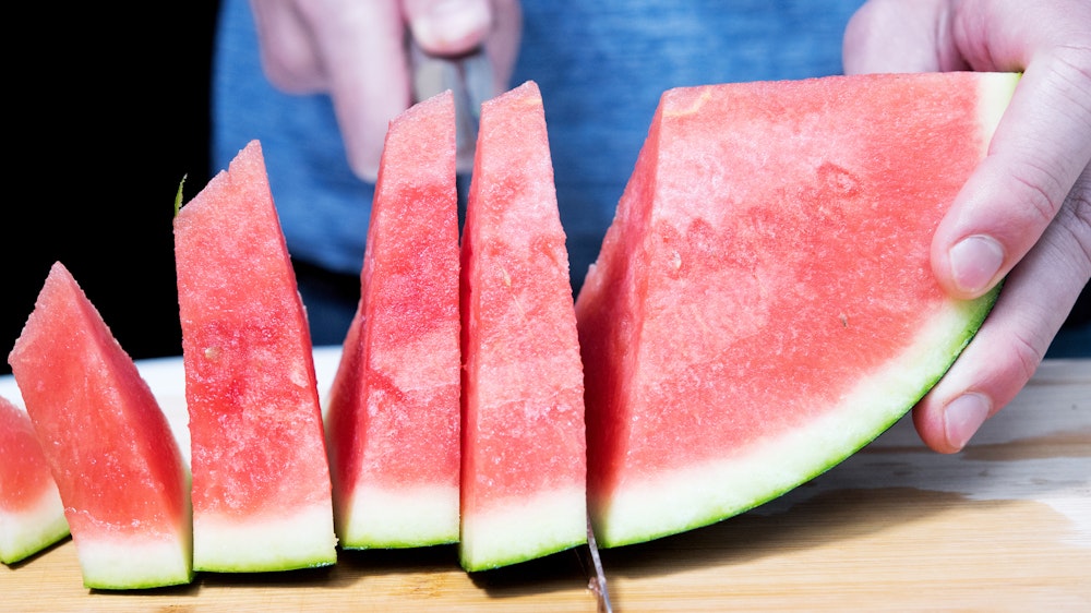 Ein Mann schneidet eine Wassermelone auf. Auch das Melonengrün – die weiße Schicht – kann man mitessen.