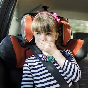 Ein Mädchen hält sich auf dem Rücksitz eines Autos die Hand vor den Mund.