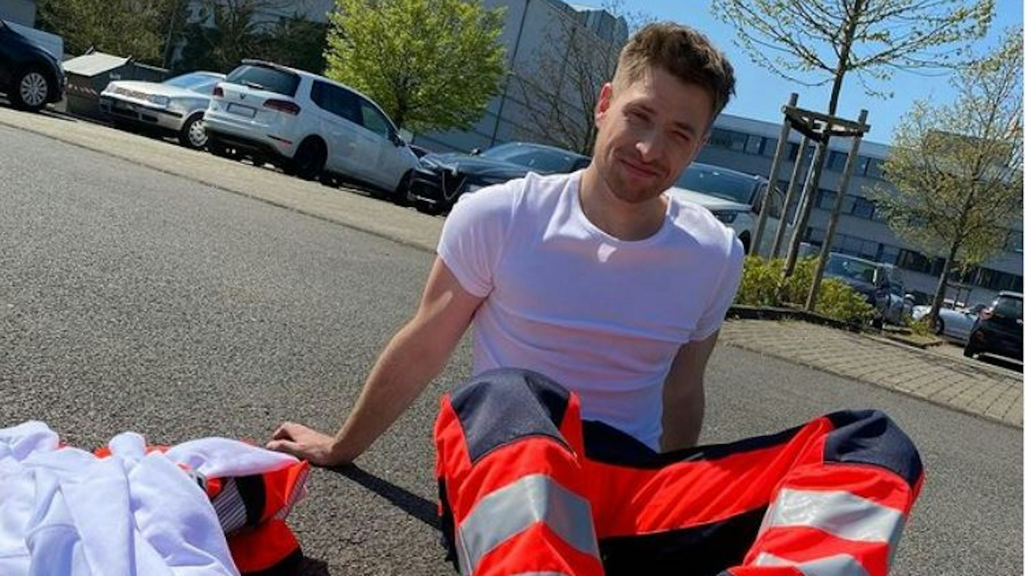 Dominik Flade sitzt in Arbeitskleidung eines Notfallsanitäters auf der Straße.