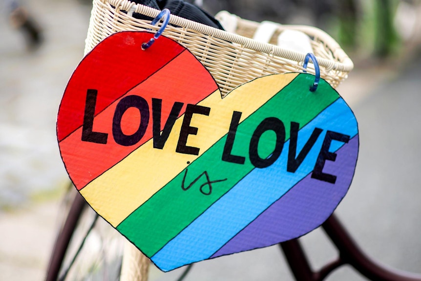 Ein herzförmiges Schild mit den Regenbogenfarben und der Aufschrift 'Love is Love'.