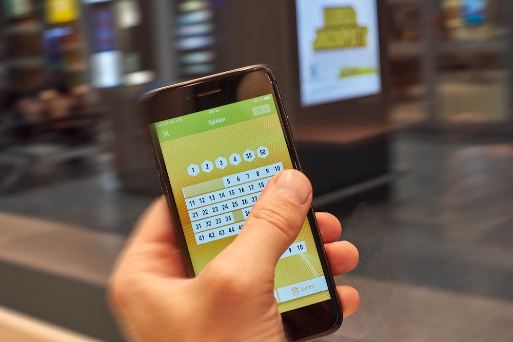 Mann hält Smartphone in der Hand und tippt Eurojackpot Lottozahlen