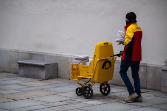 Ein DHL-Bote verteilt mit Mund-Nasen-Schutz Briefe.