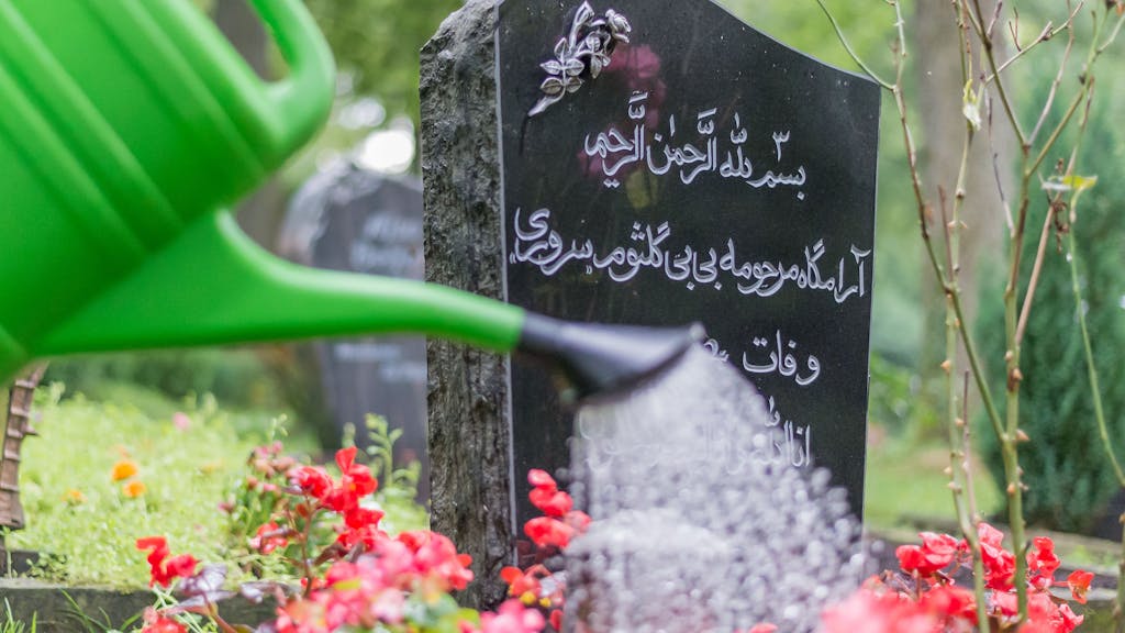 Jemand gießt die Blumen auf einem muslimischen Grab.