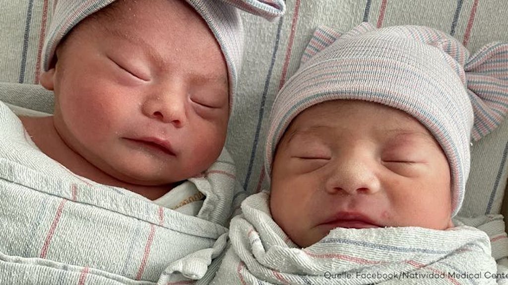 Neugeborene Zwillinge liegen nebeneinander im Kinderbett und schlafen.