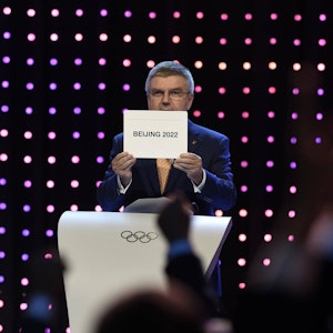 Thomas Bach hält ein Schild hoch, auf dem „Beijing 2022“ steht.