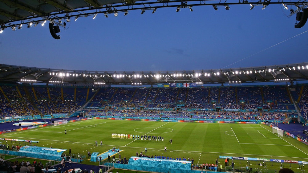 Das Stadioninnere ist aus dem Weitwinkel zu sehen. Die Mannschaft stehen auf dem Platz und lauschen den Nationalhymnen.