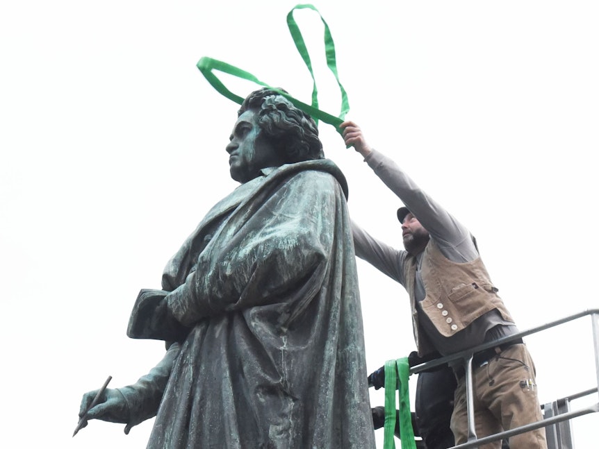 ein Mann wird der Beethoven-Statue einen Sicherheitsgurt über den Kopf.
