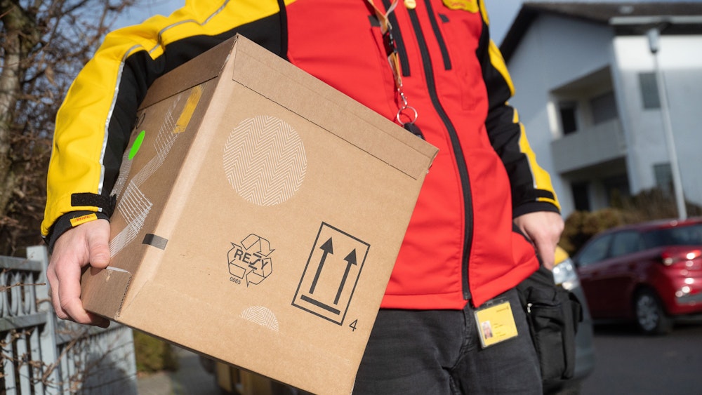 Ein DHL-Mitarbeiter trägt ein Paket unter seinem Arm. Das Symbolbild wurde am 15. Dezember 2021 aufgenommen.