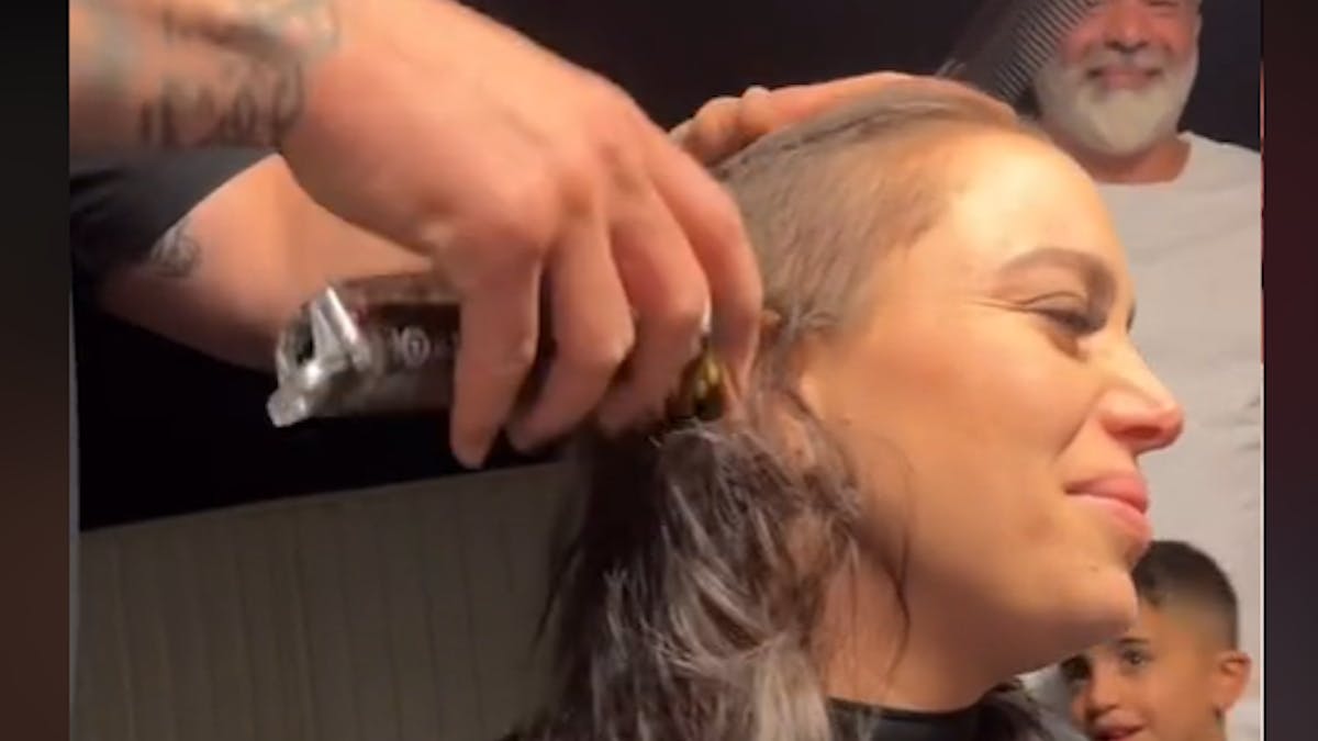 Mann rasiert den Kopf einer Frau, die das Gesicht verzehrt.