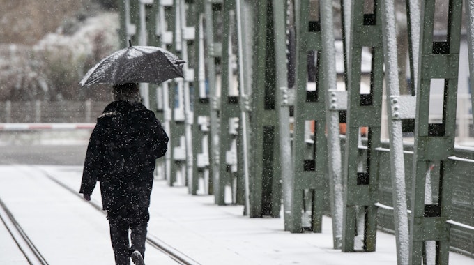 Eine Spaziergängerin mit einem Regenschirm geht bei leichtem Schneefall über eine Brücke am Hengsteysee.