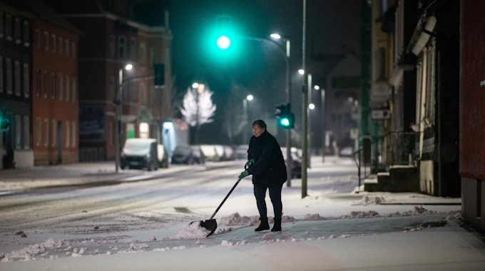 Eine Frau schippt am frühen Morgen Schnee auf dem Bürgersteig.