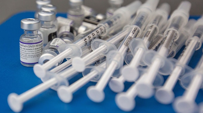 Spritzen und Fläschchen mit dem Impfstoff COVID-19 von Pfizer-BioNTech liegen auf einer Arbeitsfläche.