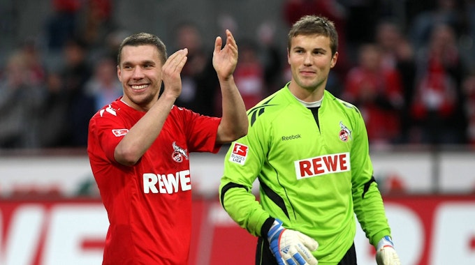 Lukas Podolski applaudiert den Fans zu, Michael Rensing steht neben ihm und lächelt.