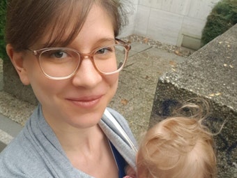 Kölnerin Alexandra Jahnz schaut in die Kamera und trägt eines ihrer Kinder auf dem Arm.