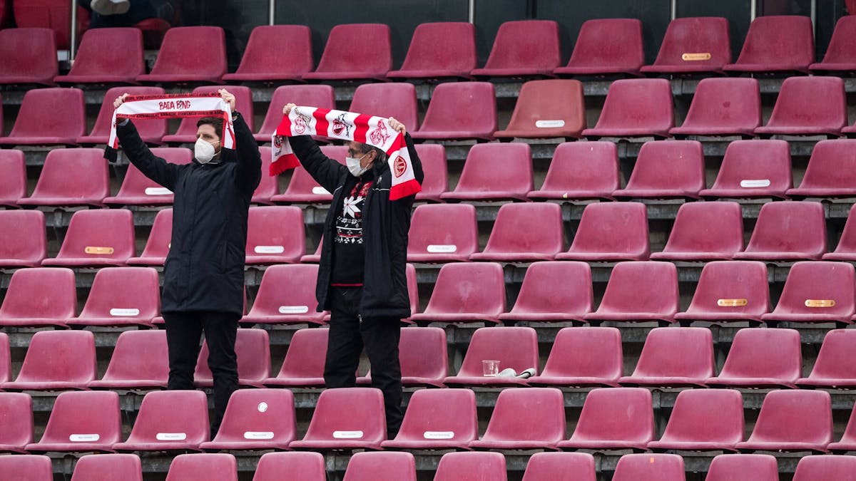 Zwei Fans des 1. FC Köln stehen auf der Tribüne und halten ihre Schals in die Höhe