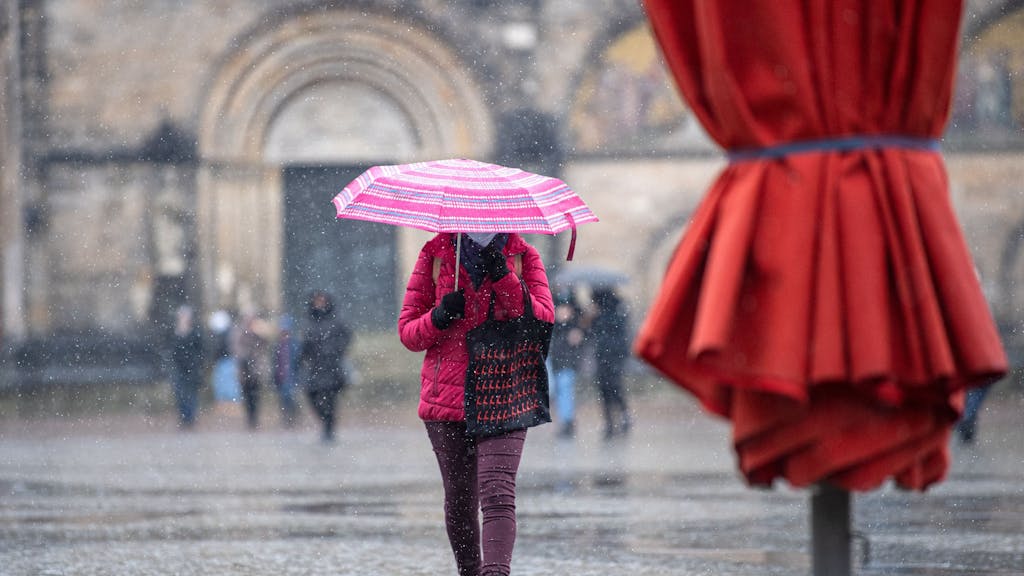 Eine Frau mit Regenschirm läuft bei Schneeregen über den Marktplatz.&nbsp;