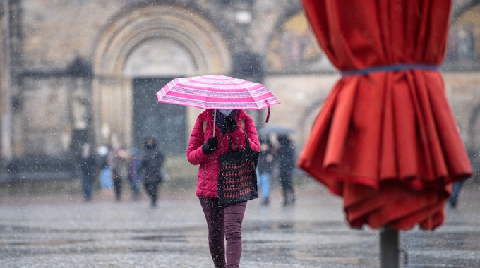 Eine Frau mit Regenschirm läuft bei Schneeregen über den Marktplatz.