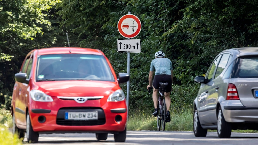 Das Bild, aufgenommen am 14. August 2021, zeigt neben dem neuen Verkehrsschild ein silbernes Auto, das den Fahrradfahrer nicht überholt, sowie ein rotes Auto auf der entgegengesetzten Fahrtseite.