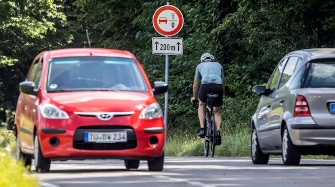 Das Bild, aufgenommen am 14. August 2021, zeigt neben dem neuen Verkehrsschild ein silbernes Auto, das den Fahrradfahrer nicht überholt, sowie ein rotes Auto auf der entgegengesetzten Fahrtseite.