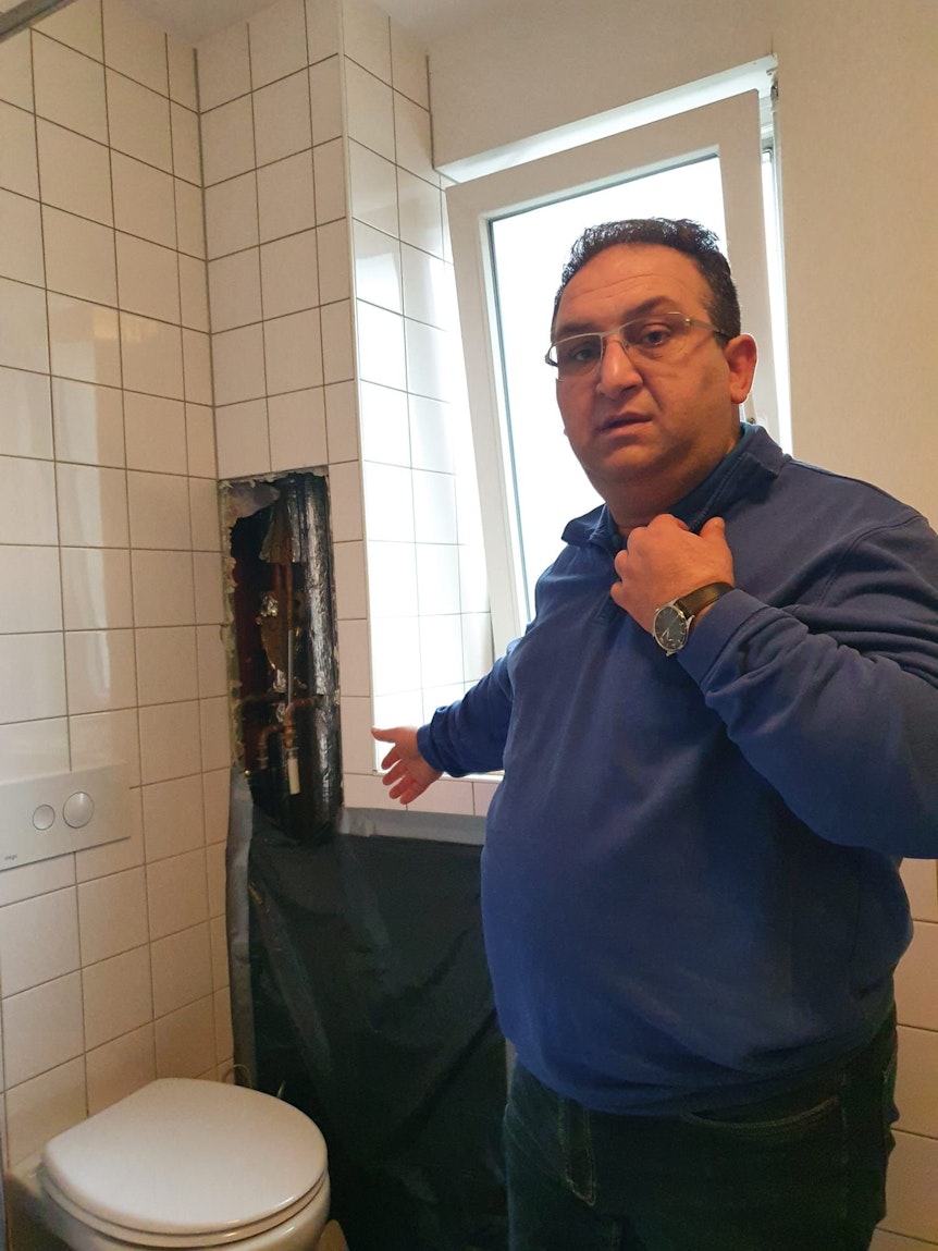 Murat Sahin steht in seinem Badezimmer und zeigt auf ein Loch in der Wand.