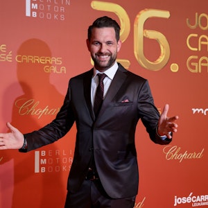 Moderator Matthias Killing kommt zur 26. Jose-Carreras-Gala. Das Bild zeigt ihn mit offenen Armen posierend vor einer Wand mit den Sponsoren der Gala.