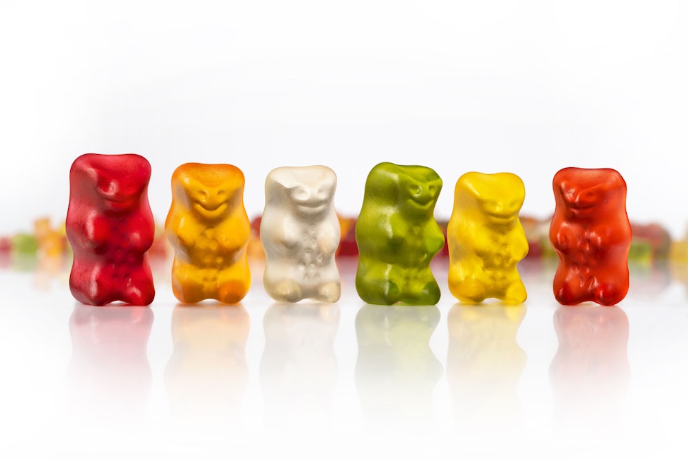Sechs Haribo Goldbären in den Farben rot, orange, weiß, grün, gelb und rot stehen nebeneinander.