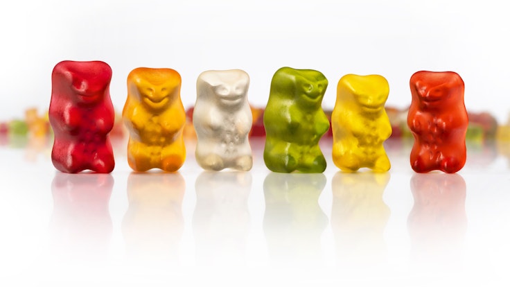 Sechs Haribo Goldbären in den Farben rot, orange, weiß, grün, gelb und rot stehen nebeneinander.