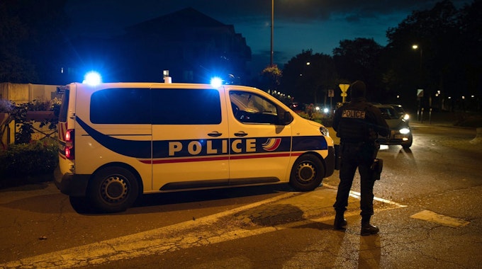 Französisches Polizeiauto steht nachts auf der Straße, daneben ein französischer Polizist. Symbolbild vom 16. Oktober 2020.