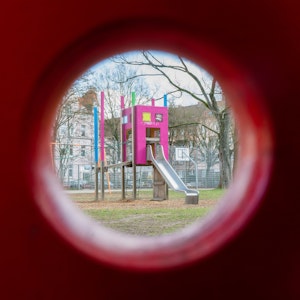 Blick durch ein Schaukelpferd auf eine Rutsche auf einem Kinderspielplatz.