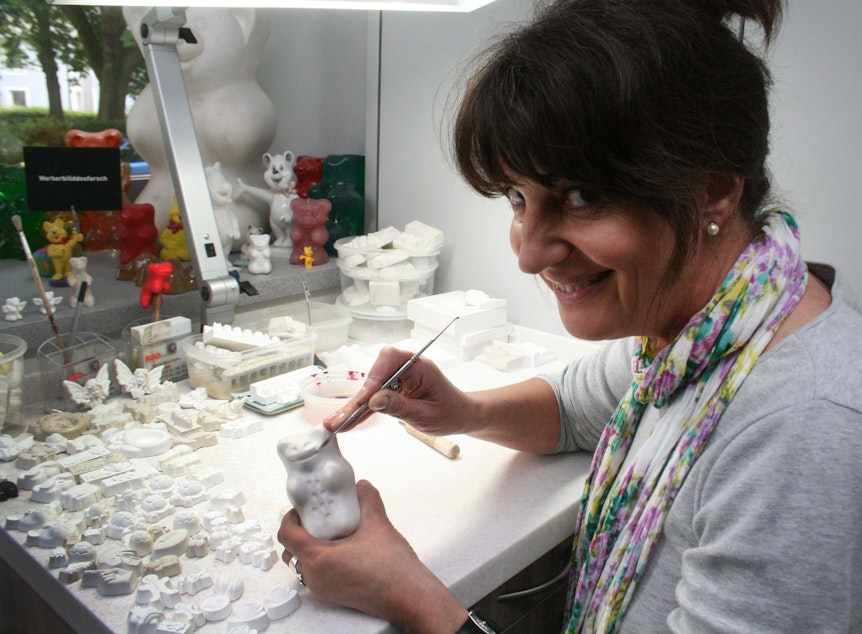 Produktdesignerin Petra Wrede hält ein Modell des Goldbären in der Hand und lächelt in die Kamera.