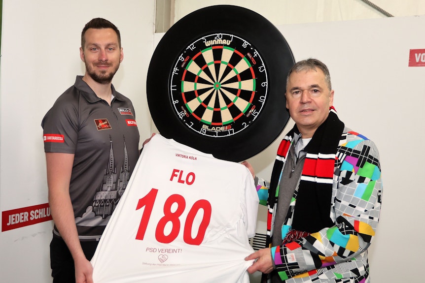 Darts-Profi Florian Hempel und Viktoria Geschäftsführer Andreas Rettig halten ein Trikot mit der Nummer 180 hoch.